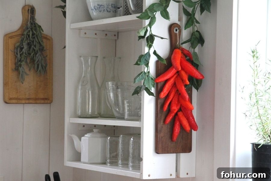 A white kitchen shelf with red peppers hanging off the end