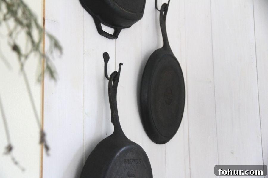 Cast iron pans hanging from hooks backed with whitewashed wood paneling