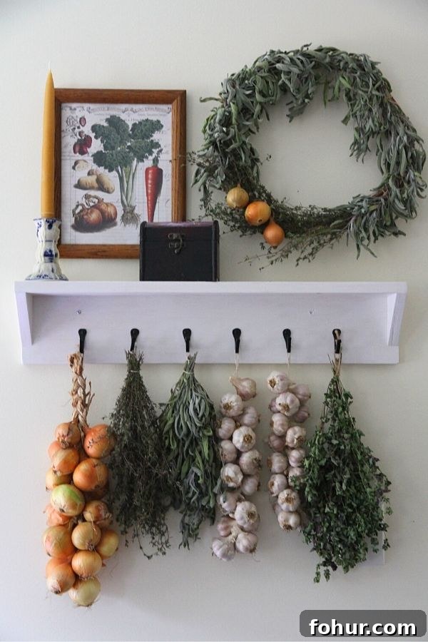 A white shelf with iron hooks displaying bundles of herbs, onions and garlic