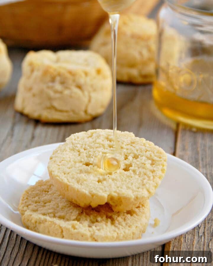 Light and Fluffy Paleo biscuits on a white plate with honey being drizzled on top on a wood table with a jar of honey in the background