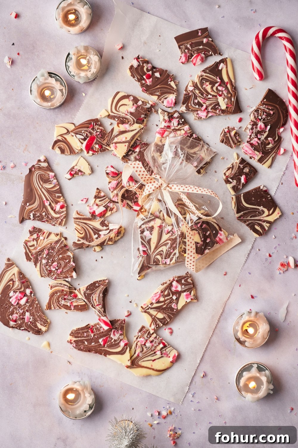 No-Bake Peppermint Bark Ready in 5 Minutes 10 Peppermint bark pieces on parchment paper. A small clear bag of peppermint bark is tied with a ribbon and sitting in the middle of the peppermint bark pieces.