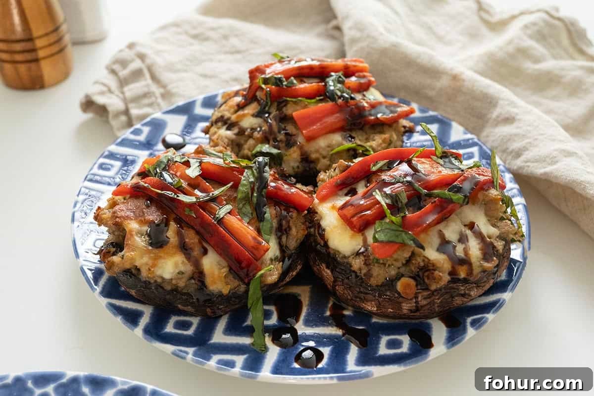 Italian-Style Baked Stuffed Portobello Mushrooms 2 Baked Italian stuffed portobello mushrooms topped with roasted red peppers, basil and balsamic glaze on a plate.