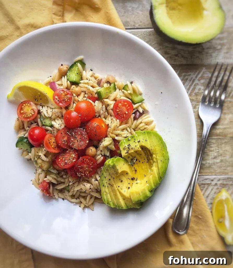 Vegan Greek Orzo Salad with Lemon and Olives 2 overhead view of a greek inspired vegan orzo salad on a white dish with cherry tomatoes, avocado, red onion, cucumbers, and lemon.