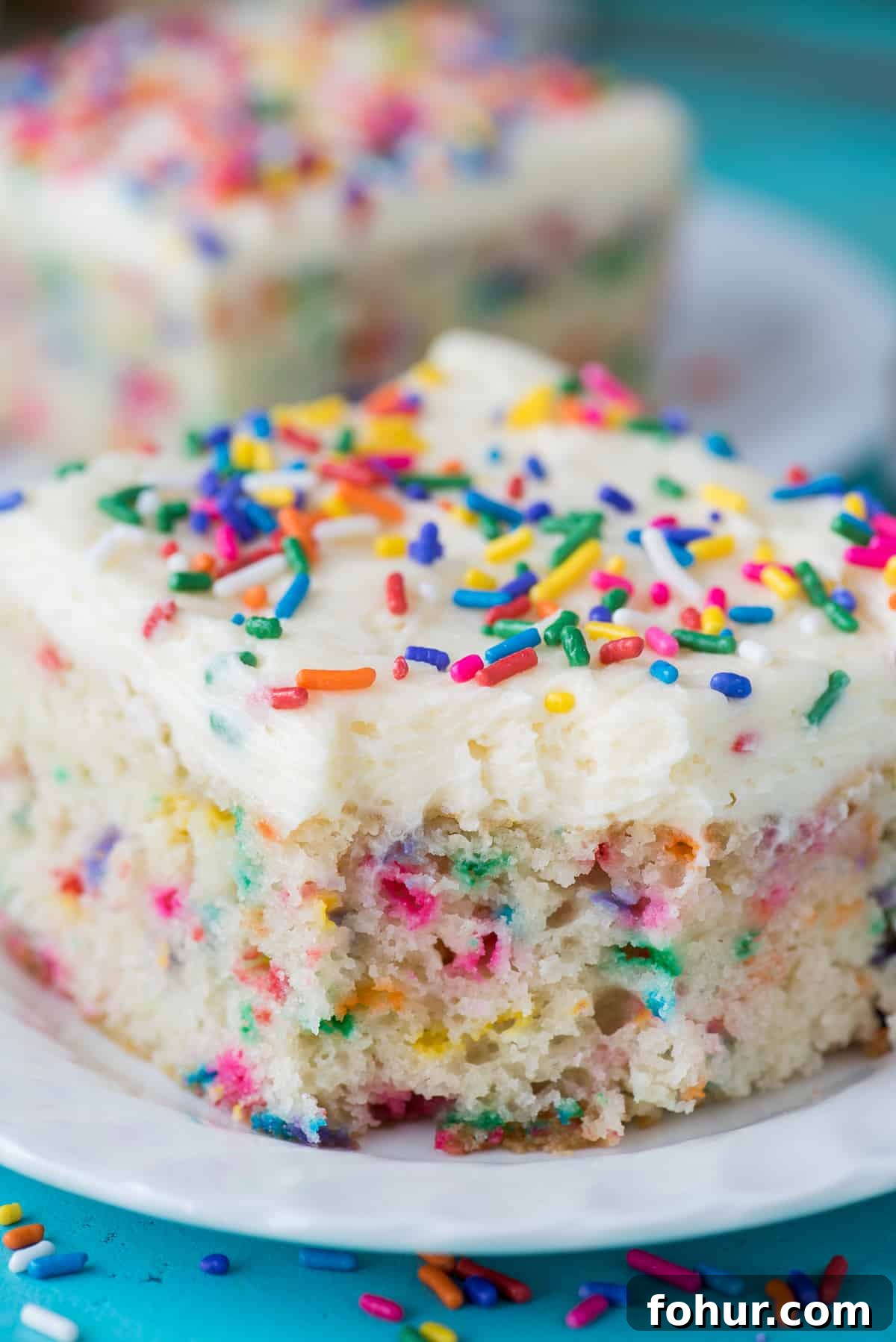 How to Make a Classic Funfetti Cake 6 piece of funfetti cake with bite removed on white plate on teal background