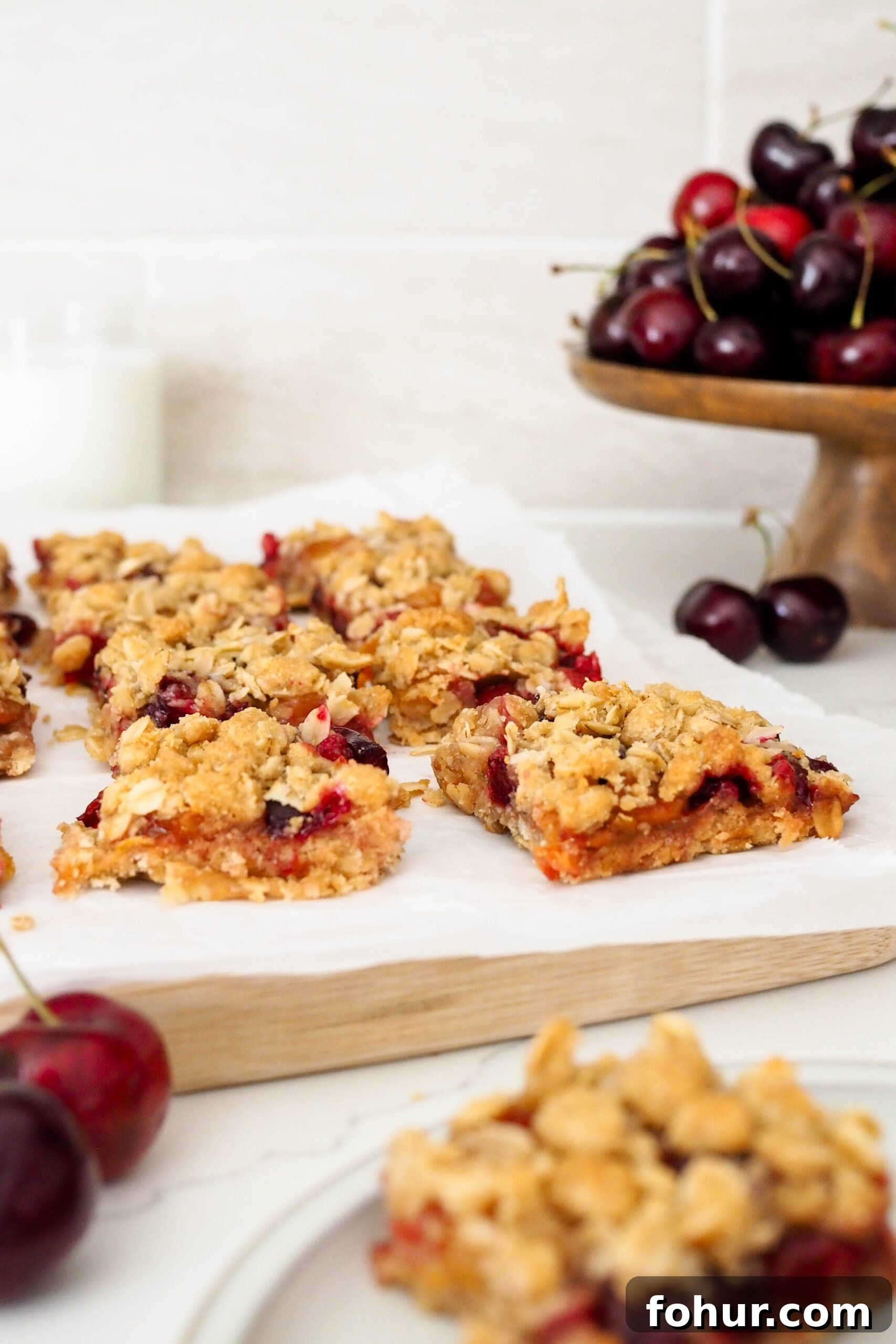 Cherry Crumble Bars with Buttery Oat Crust 12 A batch of cherry crumble bars on parchment near cherries.