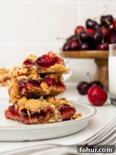 Cherry Crumble Bars with Buttery Oat Crust 14 Three cherry crumble bars are stacked on a plate.