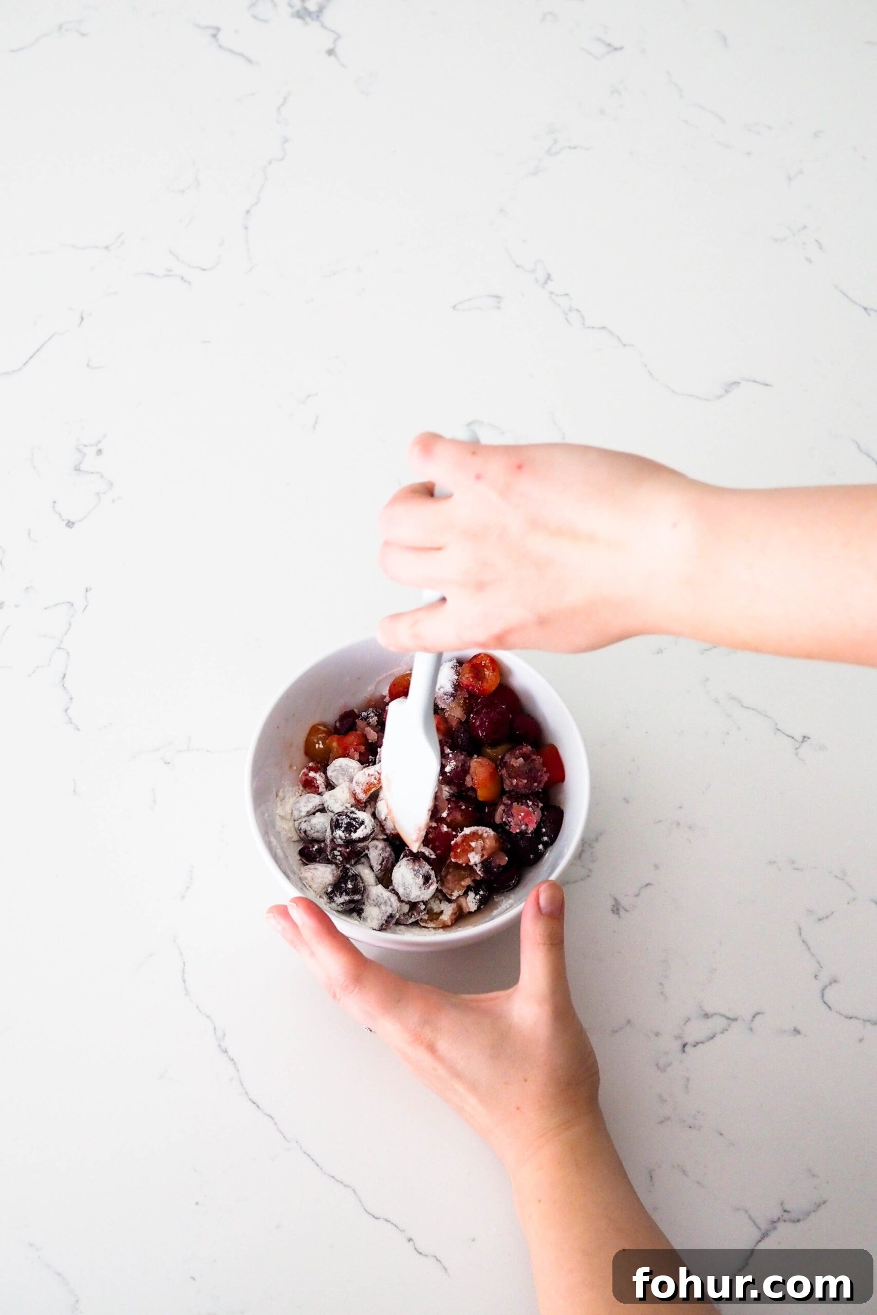 Cherry Crumble Bars with Buttery Oat Crust 4 Two hands stir together cherries, sugar, vanilla extract, and flour in a glass bowl.
