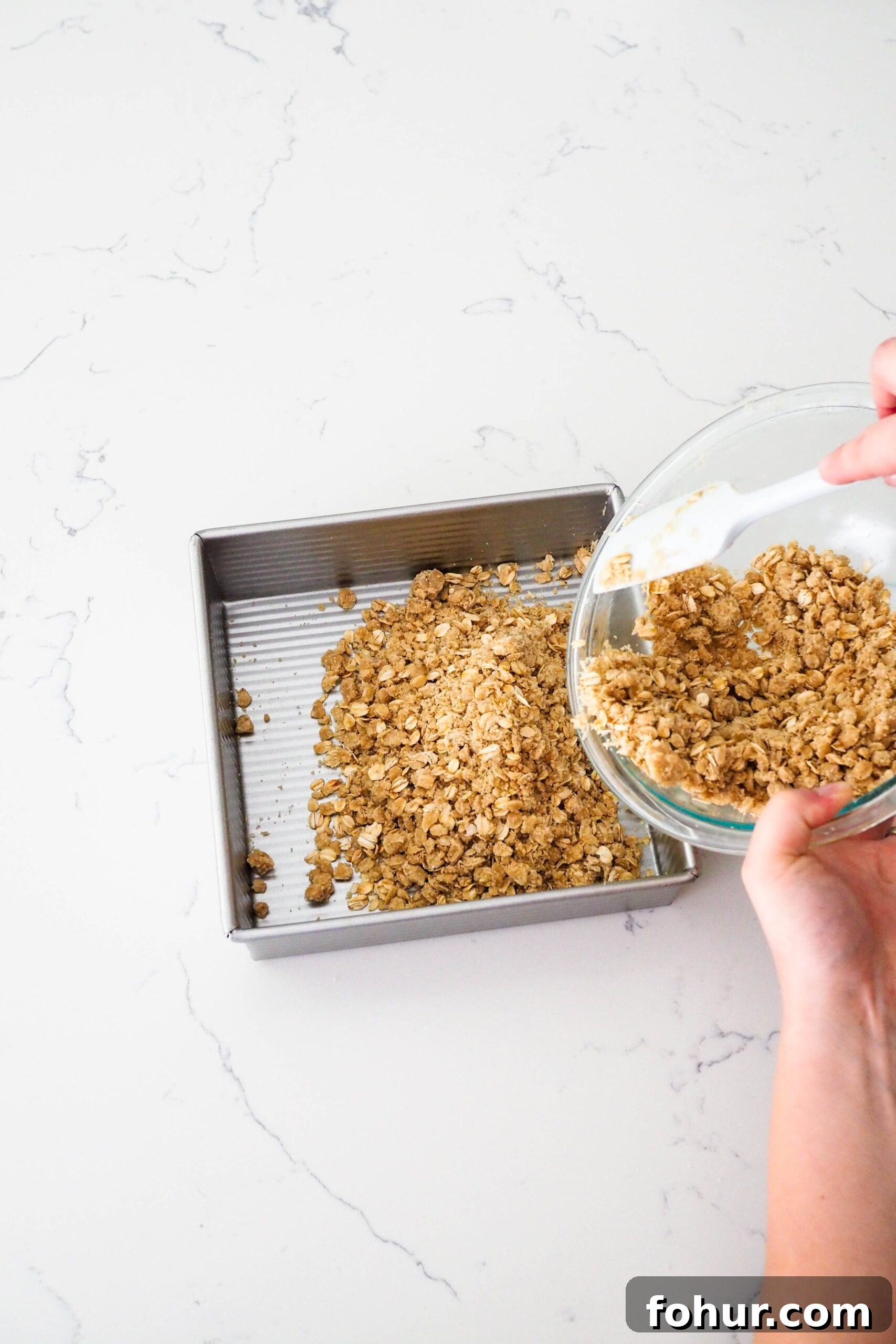 Cherry Crumble Bars with Buttery Oat Crust 7 Two hands pour an oat crumble crust into a square pan.