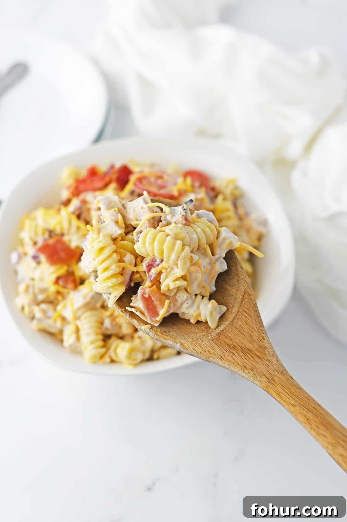 A spoonful of pasta salad with chicken, bacon and tomatoes.