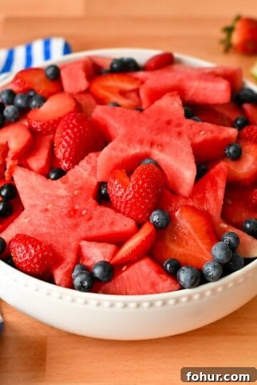 Red white and blue fruit salad with watermelon stars, sliced strawberries, and blueberries in a white bowl.