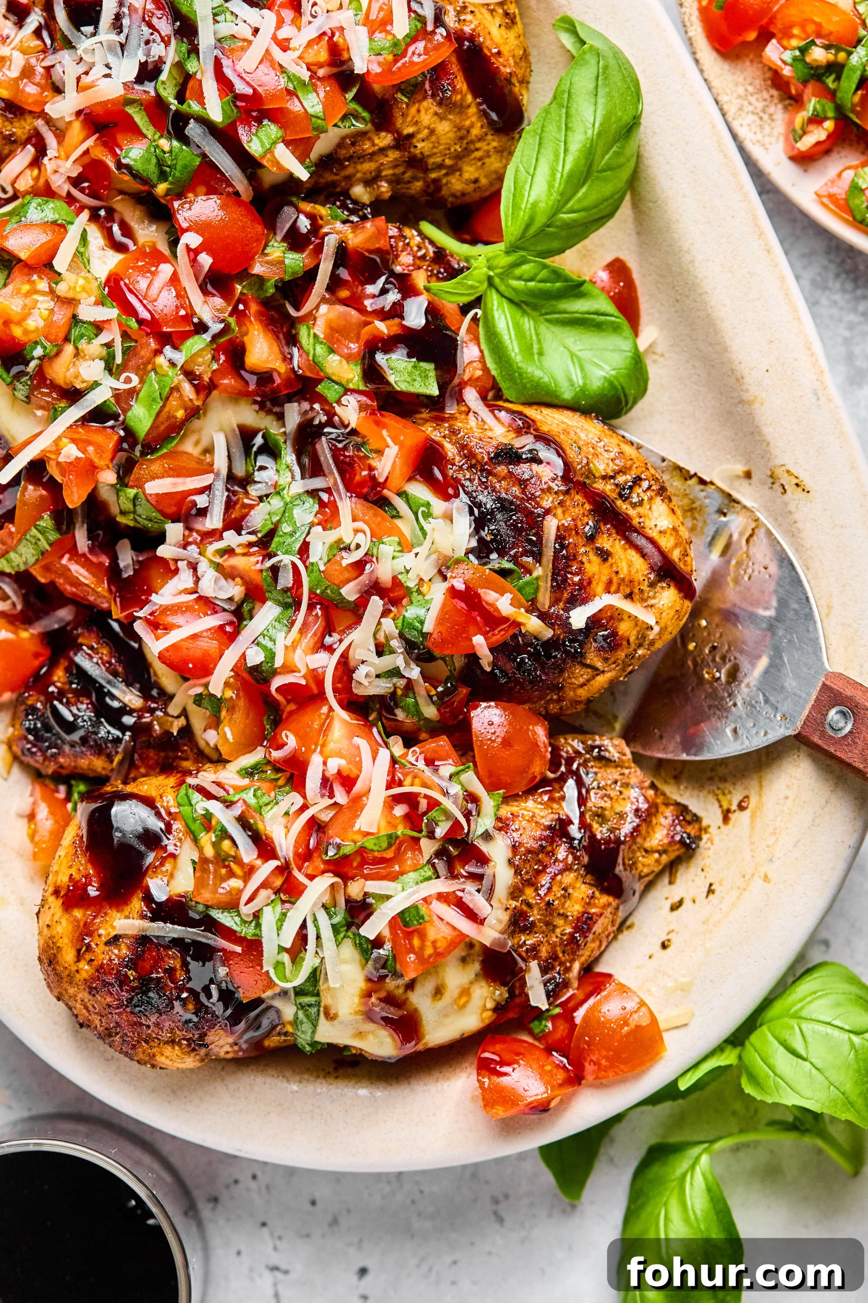 Bruschetta Chicken Recipe with Mozzarella and Balsamic Glaze 5 A serving tray filled with grilled bruschetta chicken drizzled with balsamic glaze sitting next to a small plate filled with bruschetta