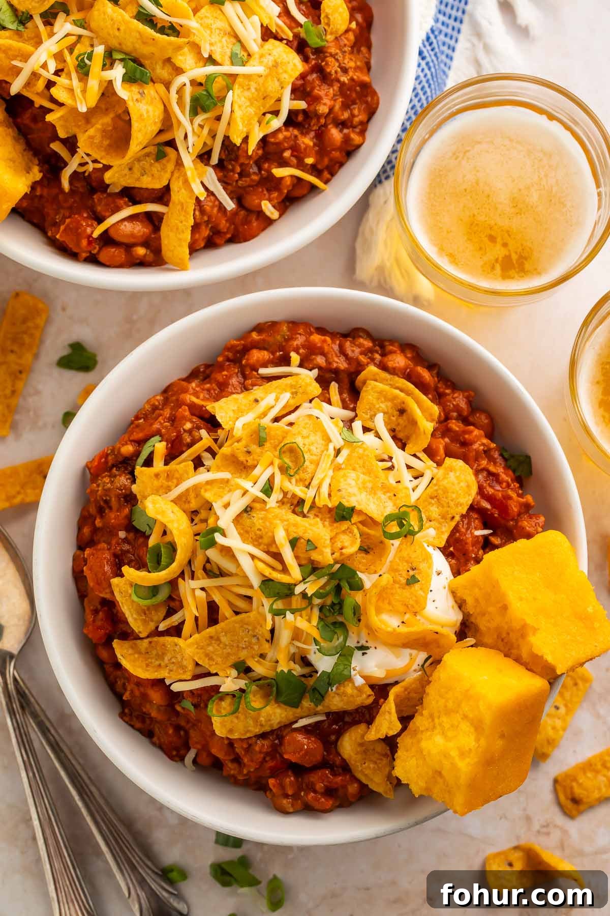 Two bowls of boilermaker chili topped with corn chips and two squares of cornbread, photographed from above.
