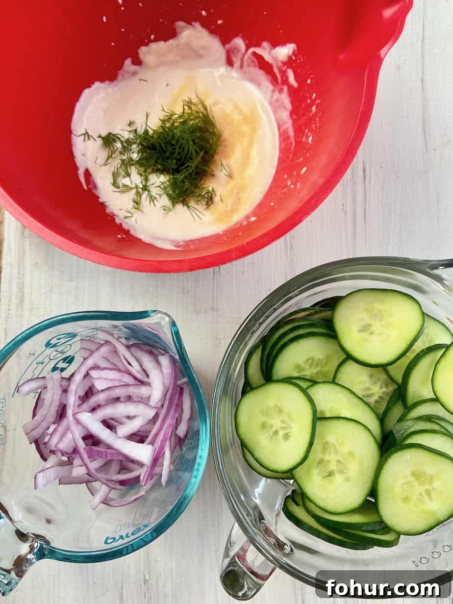 Creamy Cucumber Salad with Greek Yogurt and Dill 4 A bowl of sliced cucumbers, a bowl of sliced onions and a red bowl with the dressing ingredients.