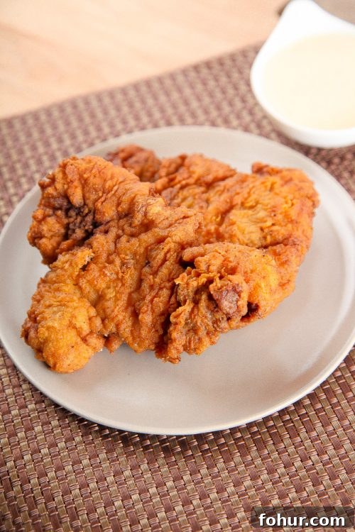 Crispy Southern Chicken Fried Steak Recipe 2 Chicken Fried Steak on an off white plate with a bamboo placement.