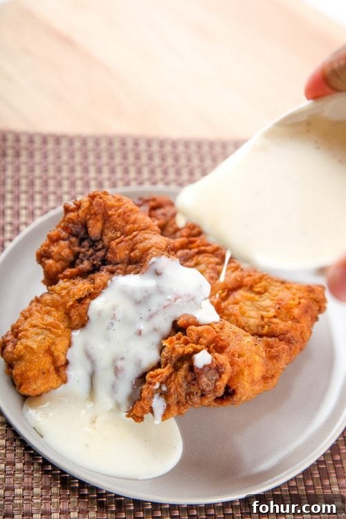 Crispy Southern Chicken Fried Steak Recipe 4 a gravy boat pouring white gravy over chicken fried steak.