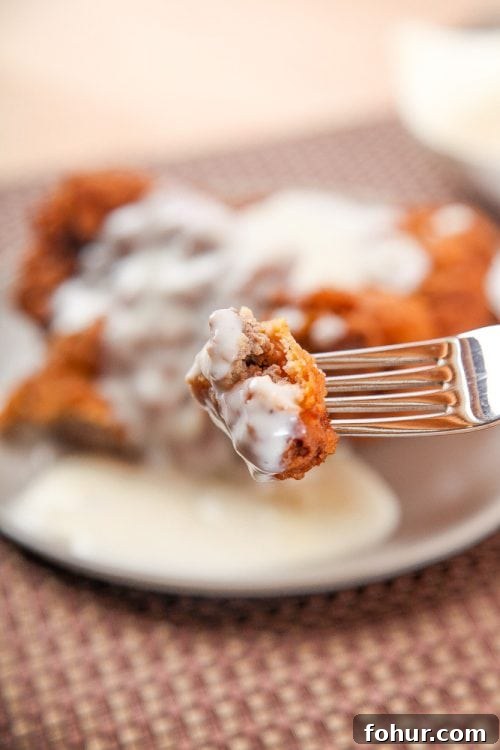 Crispy Southern Chicken Fried Steak Recipe 5 a bite of chicken fried steak with white gravy on a silver fork.