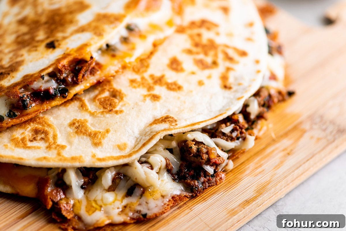 Cheesy Ground Beef Quesadillas stacked on wood cutting board.