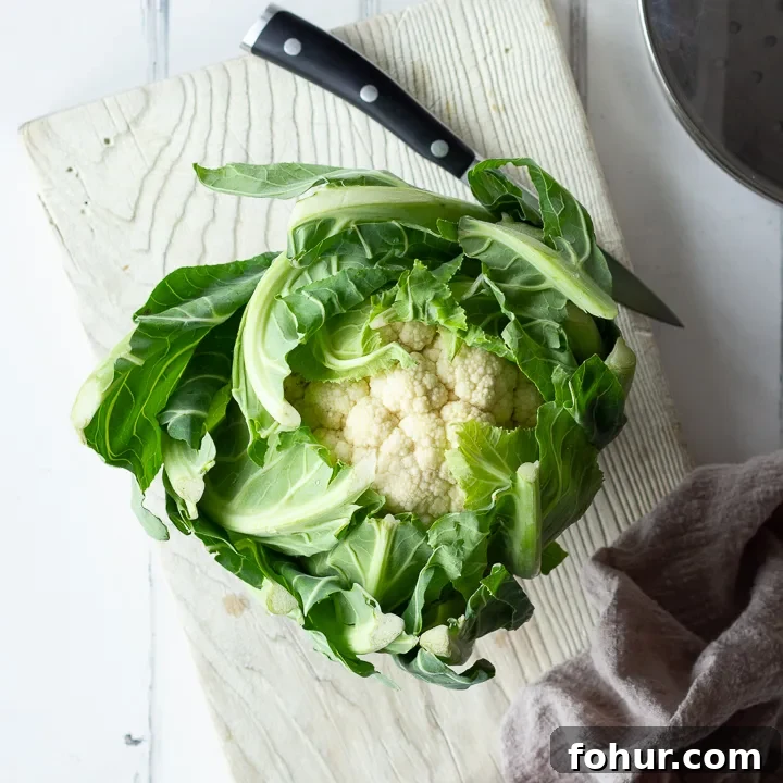 A whole cauliflower on a chopping board with a knife