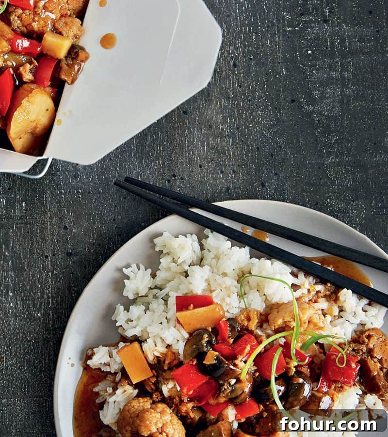 Slow Cooker Kung Pao Cauliflower served on top of a plate of white rice with chopsticks and a box of the dish on the side placed on gray matte linen