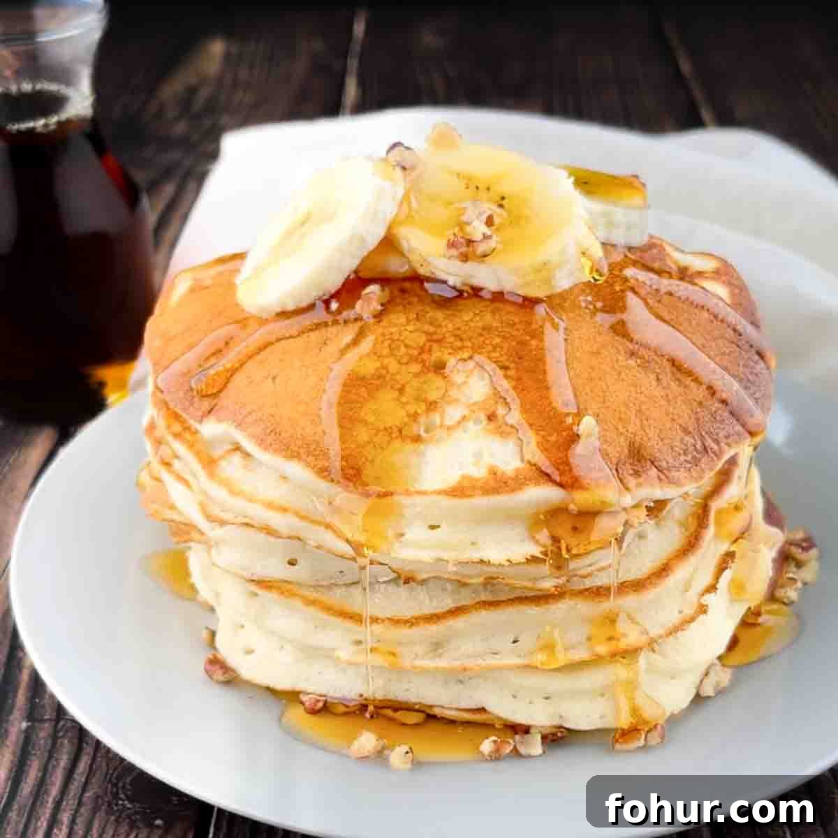 How to Make Fluffy Banana Pancakes 11 The fluffy banana pancakes on a plate and drizzled with maple syrup and topped with chopped pecans and sliced banana.