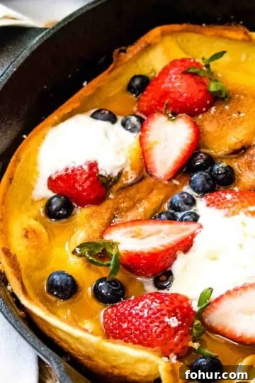 A Dutch baby pancake in a cast iron skillet with lemon sugar and fresh berries.