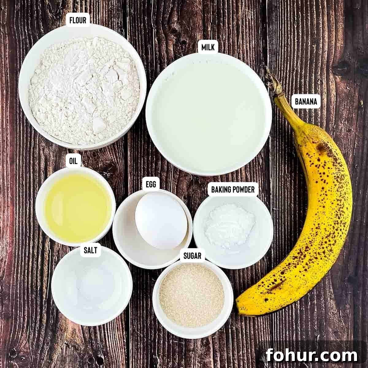 How to Make Fluffy Banana Pancakes 2 Ingredients for banana pancakes measured out and placed on a wooden table.