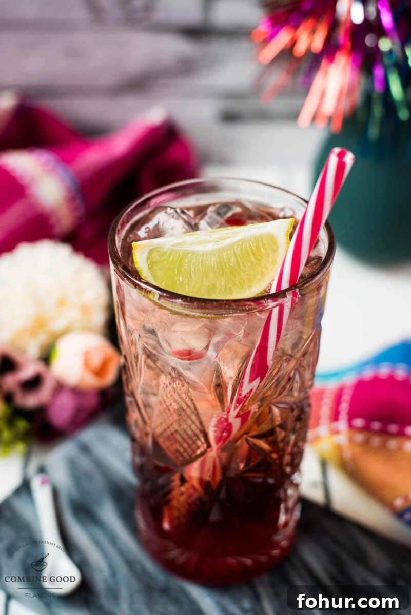 Raspberry Gin and Tonic Cocktail Recipe 8 Highball glass filled with raspberry gin and tonic, garnished with a lime wedge and a straw.