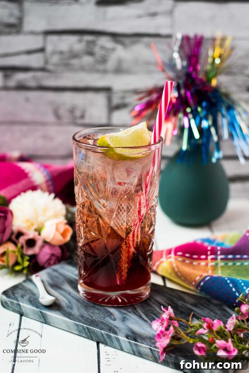 Raspberry Gin and Tonic Cocktail Recipe 9 Highball glass filled with raspberry gin tonic, garnished with a lime wedge and a straw.
