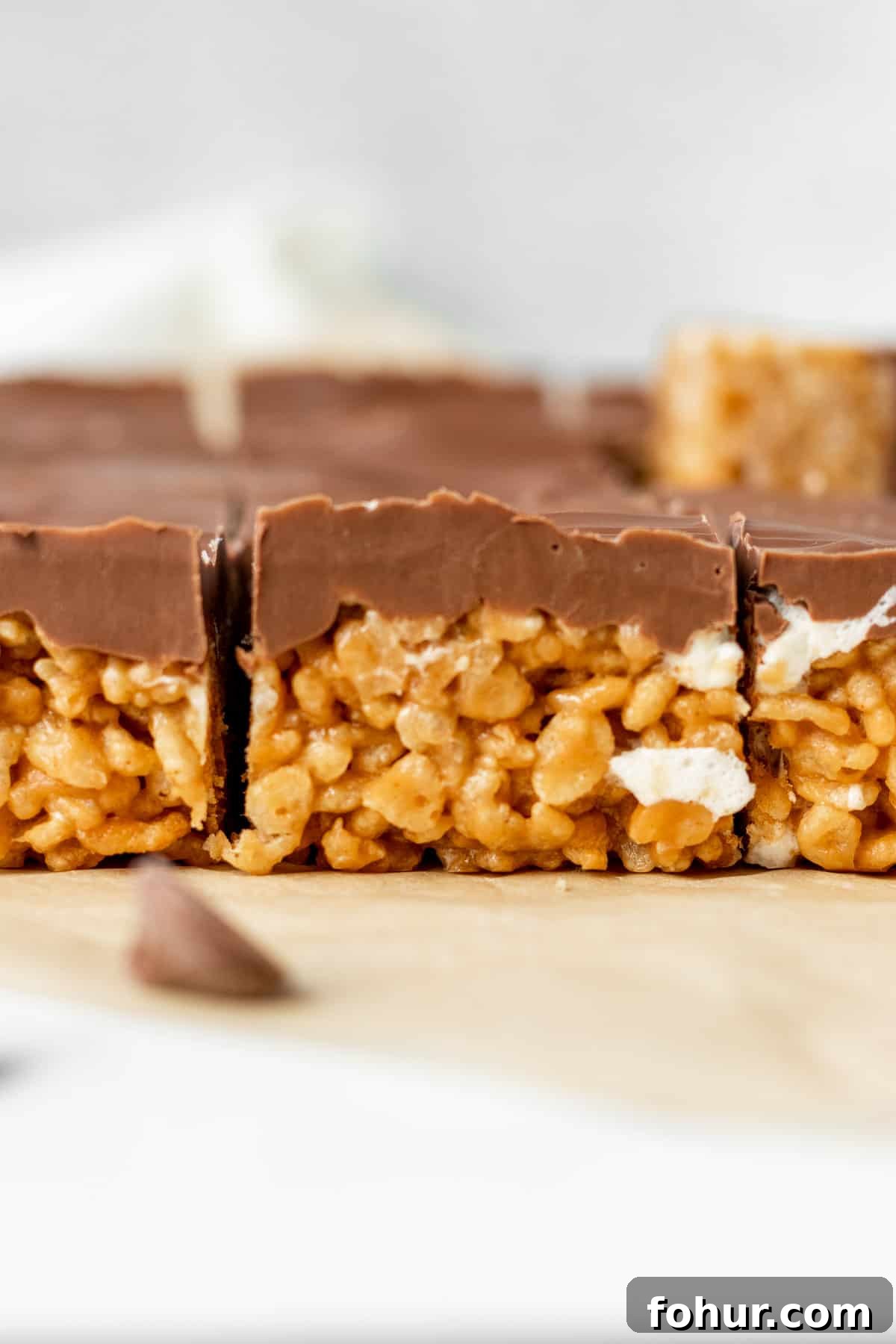 peanut butter rice krispie treats topped with chocolate sitting on brown parchment paper