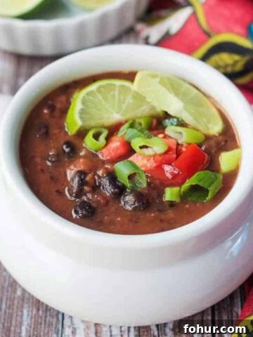 Bowl of black bean soup topped with diced tomatoes and two lime wedges.