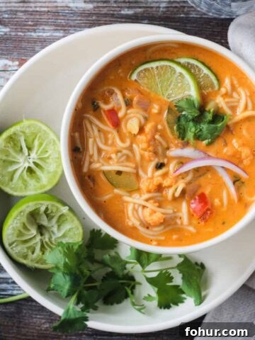Red Curry Thai Noodle Soup in a white bowl next to two lime halves and cilantro leaves.