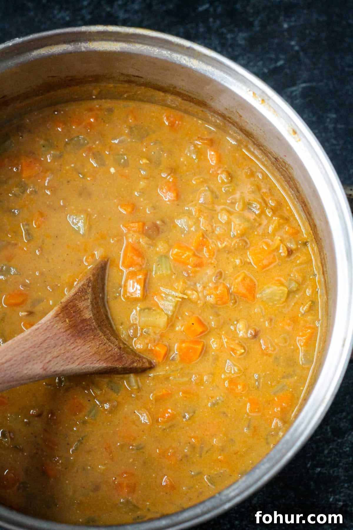 Curried Carrot and Lentil Soup Recipe 8 Close up of carrot lentil soup in a pot with a wooden spoon.