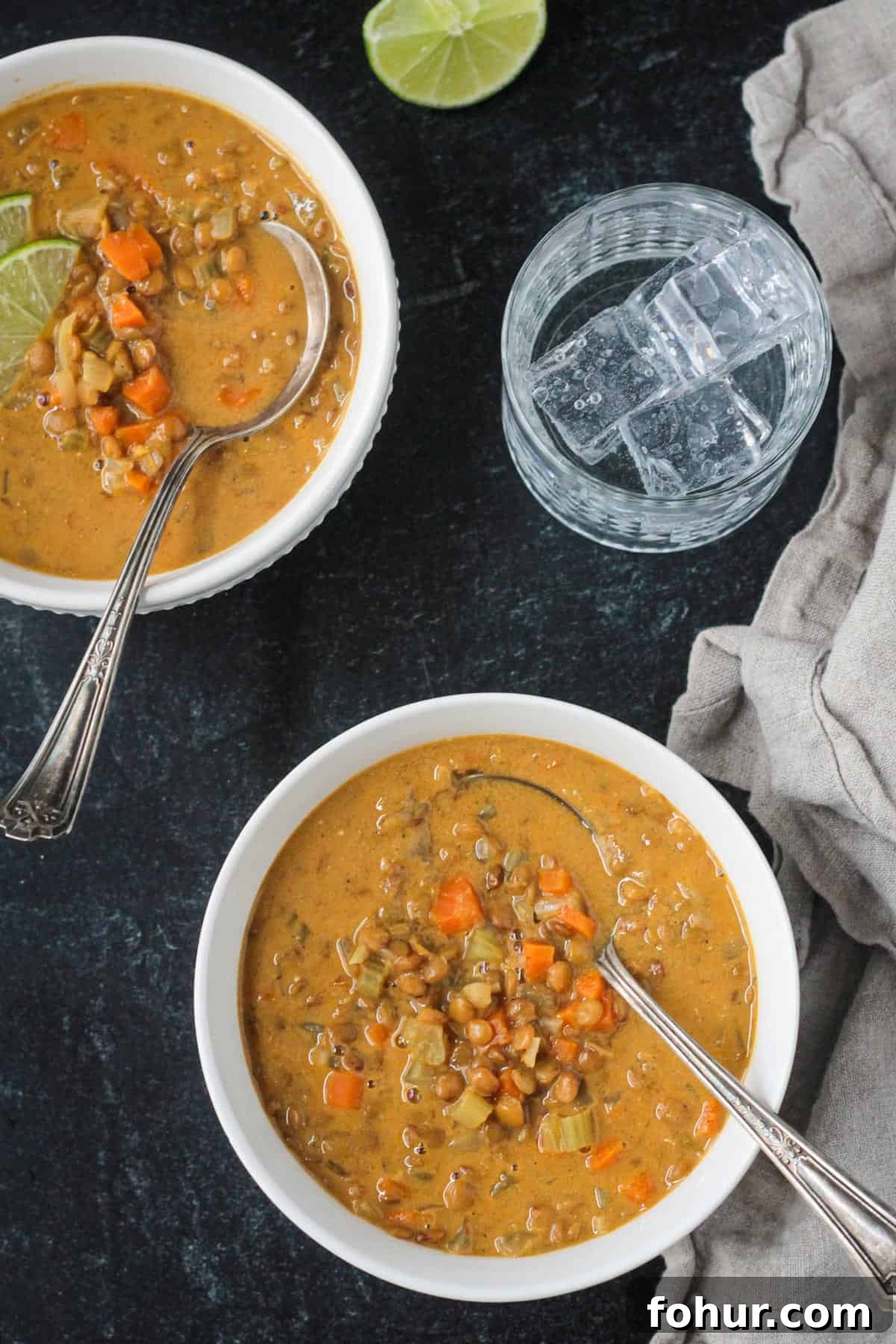 Curried Carrot and Lentil Soup Recipe 9 Two bowls of soup on table next to a glass of ice water.