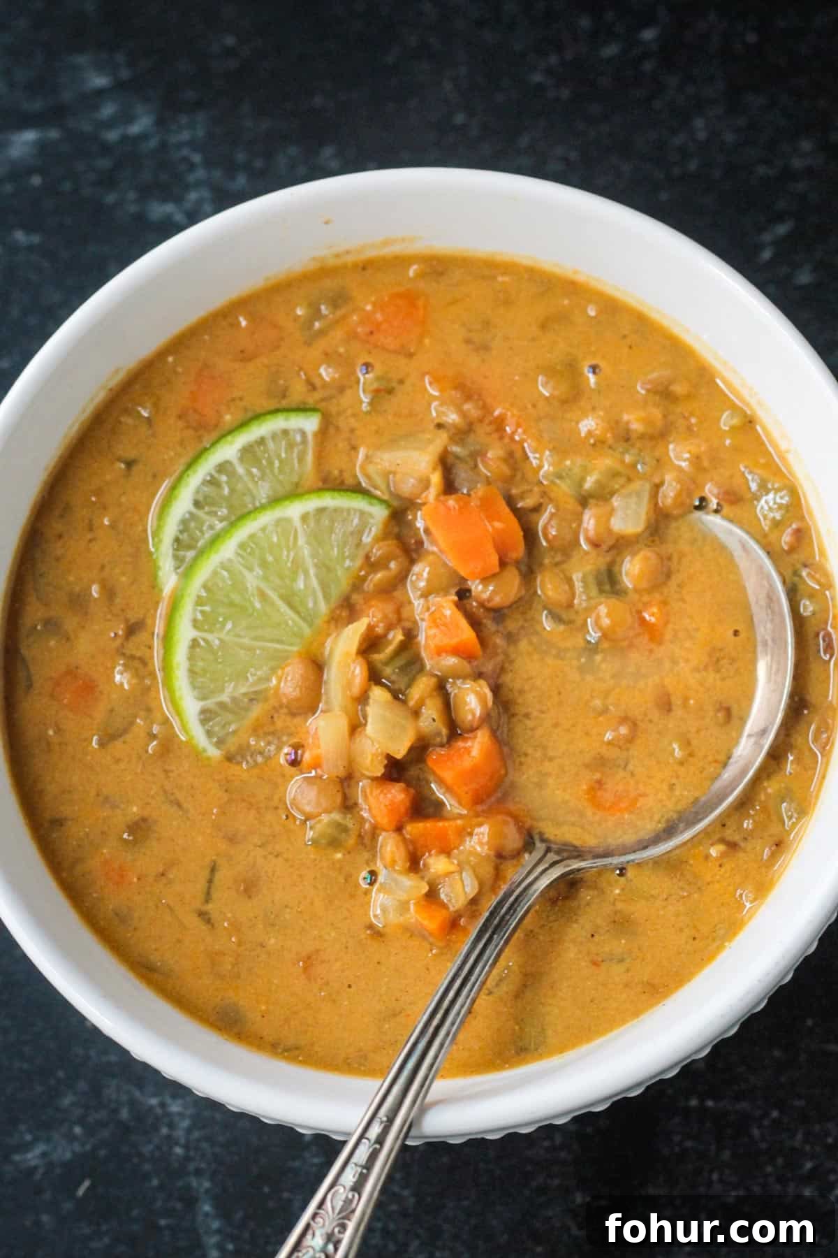 Curried Carrot and Lentil Soup Recipe 10 Metal spoon in a bowl of lentil soup garnished with two lime wedges.