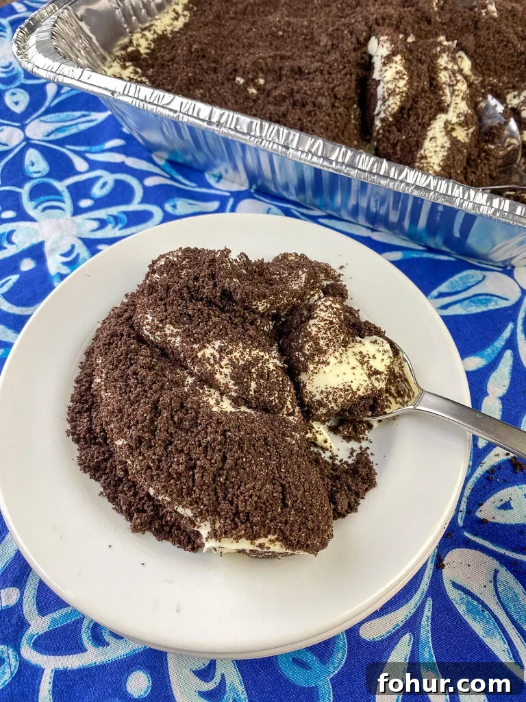 Dirt Cake Recipe to Feed a Crowd 2 Spoon full of delicious dirt cake on a white plate full of the Oreo covered pudding dessert next to a large pan full on a blue and white napkin
