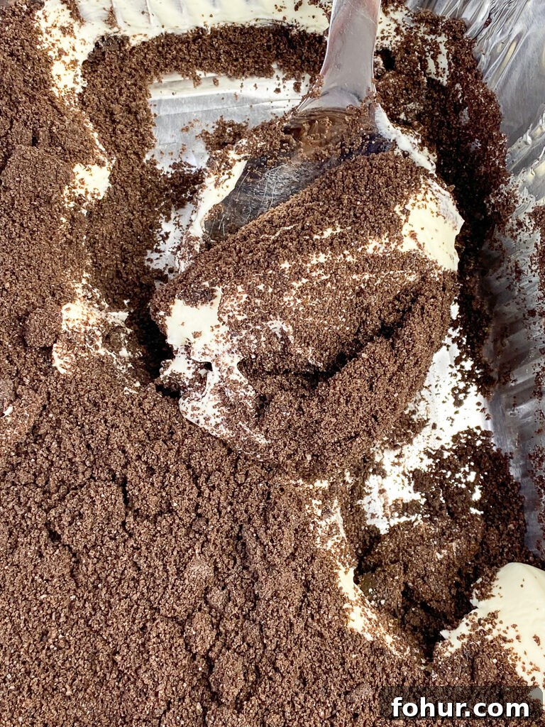 Dirt Cake Recipe to Feed a Crowd 3 Long handled silver serving spoon scooping into the layers of Oreo cookie crumbs and the creamy filling in this dirt cake dessert