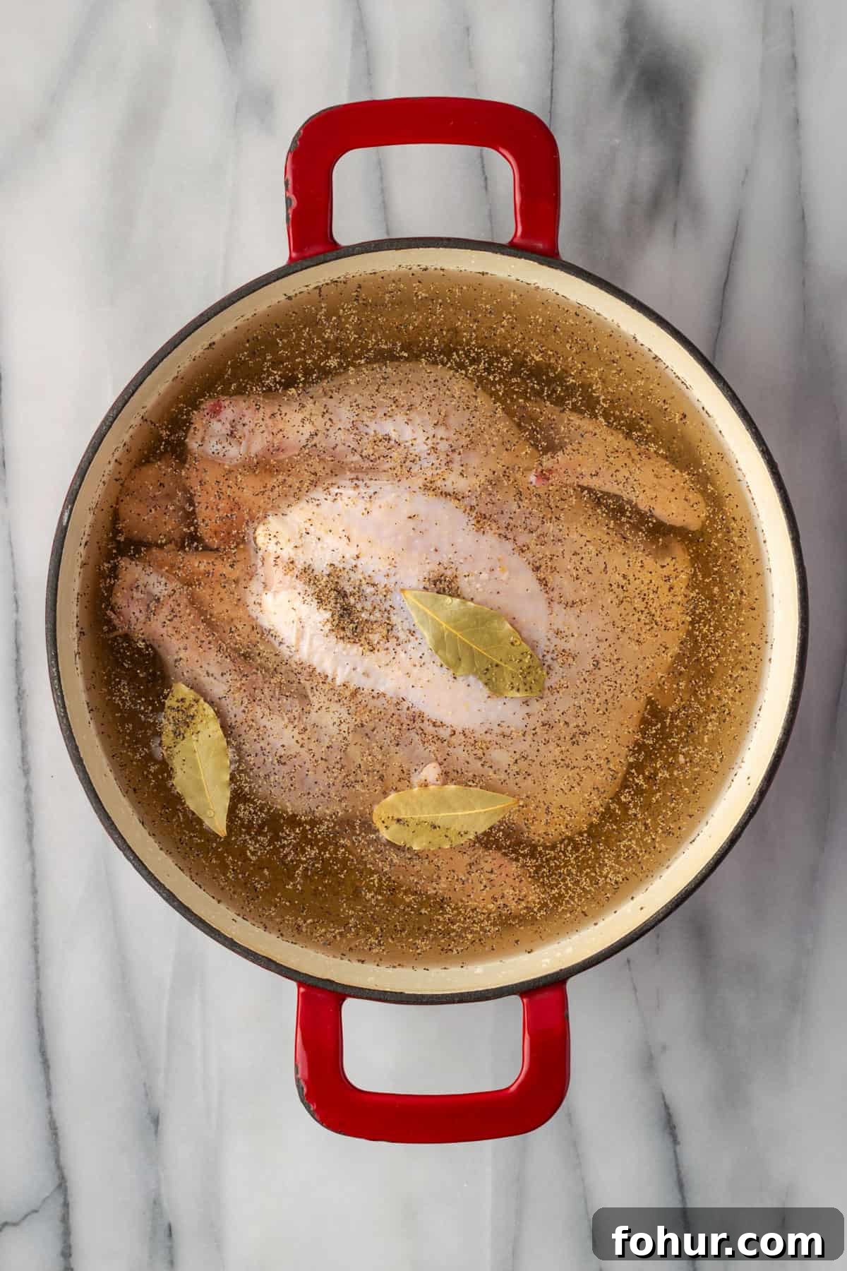 A whole chicken, salt, black pepper, bay leaves and water in a large dutch oven pot.