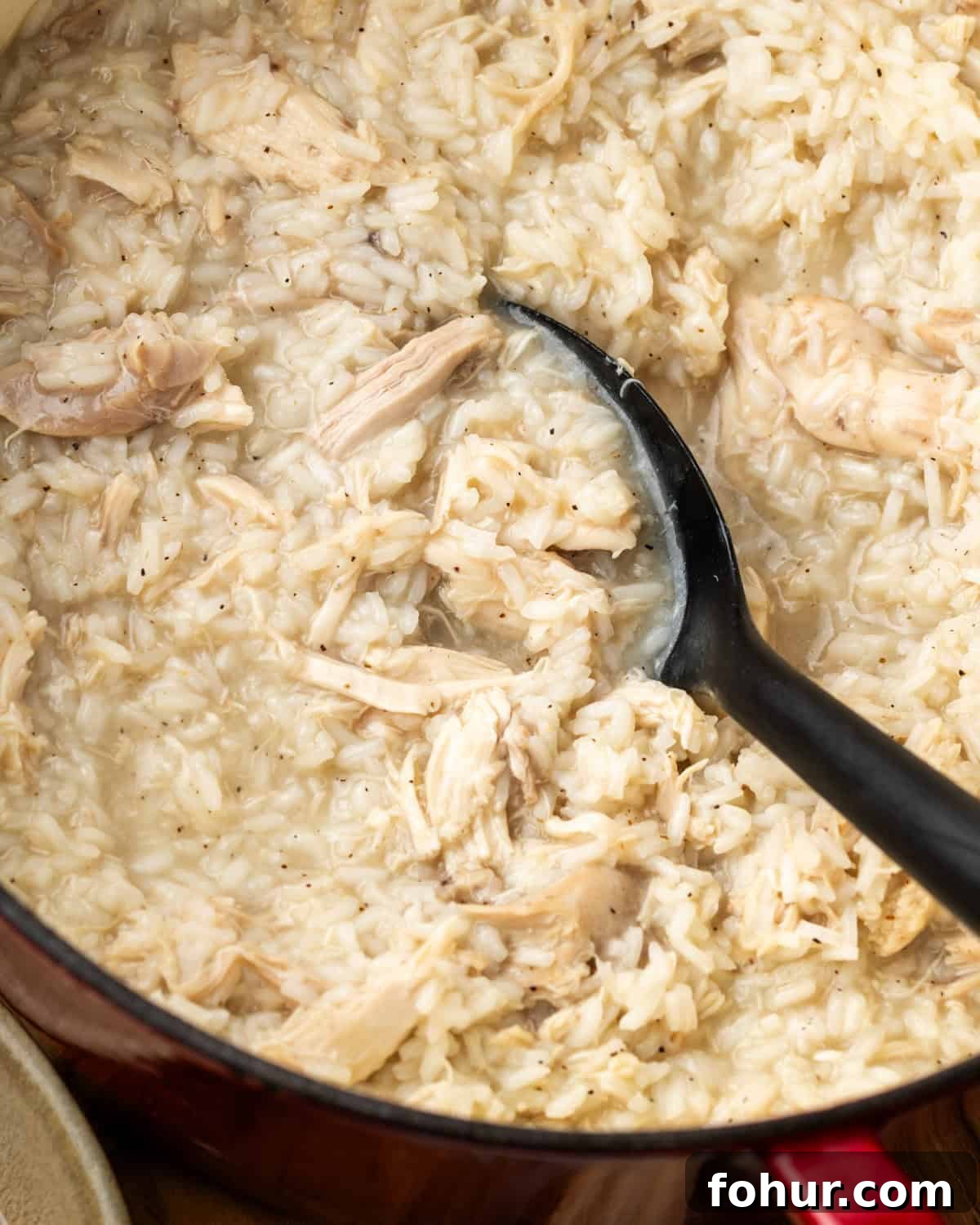 A large serving spoon scooping up chicken and rice from a big pot.