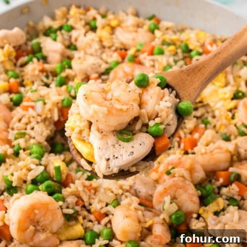 A wooden spoon scooping a serving of shrimp and chicken fried rice from the skillet.