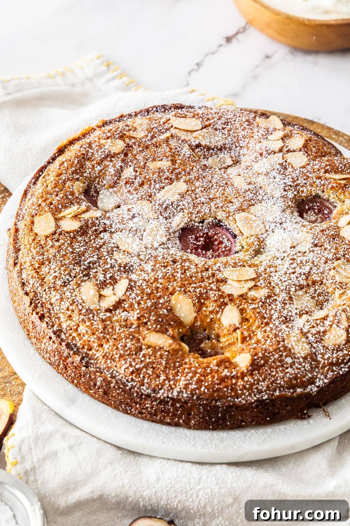 Whole Gluten-Free Fig Cake dusted with icing sugar, on a white plate, sitting on a white cloth.