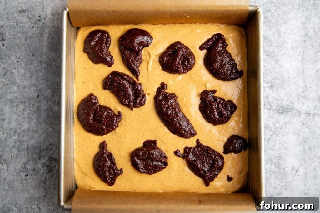Fudgy Pumpkin Cheesecake Swirl Brownies Recipe 7 cheesecake filling atop the brownie batter in the brownie pan with drops of brownie batter on top waiting to be swirled