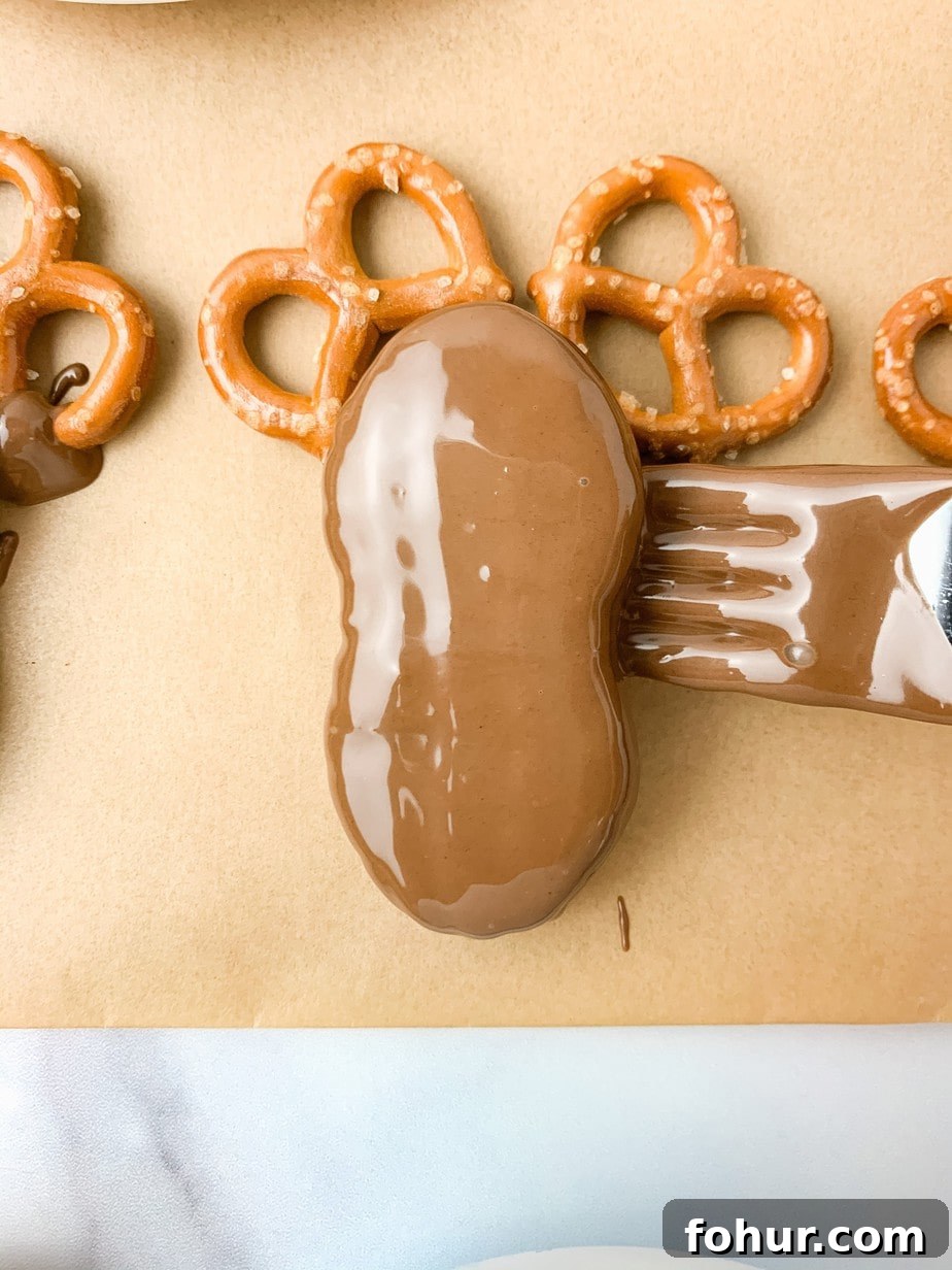 A chocolate dipped Nutter Butter being placed on two pretzels with a fork, on brown parchment paper.