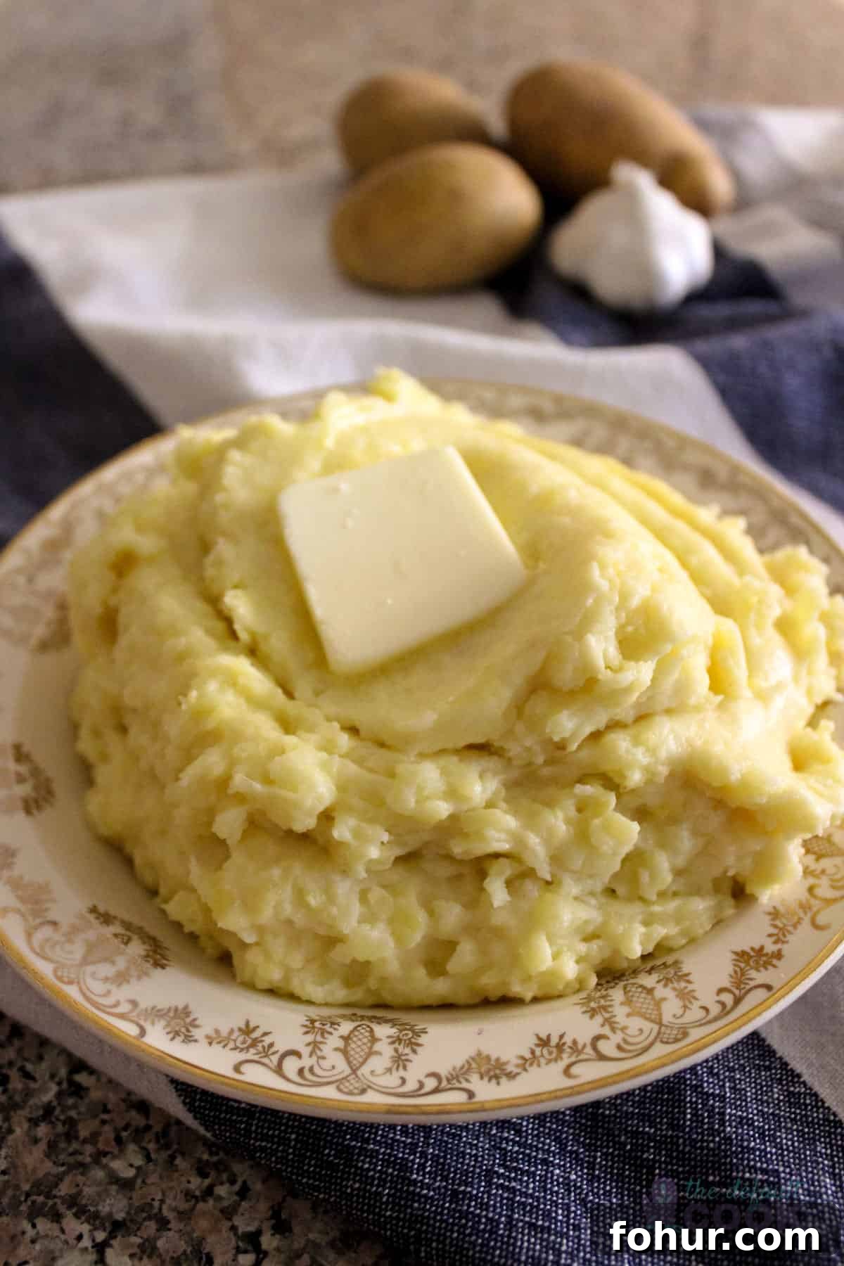 Creamy Garlic Mashed Potatoes Made in an Air Fryer 2 Plate of air fried mashed potatoes with a pat of butter melting on top, potatoes and garlic in the background.