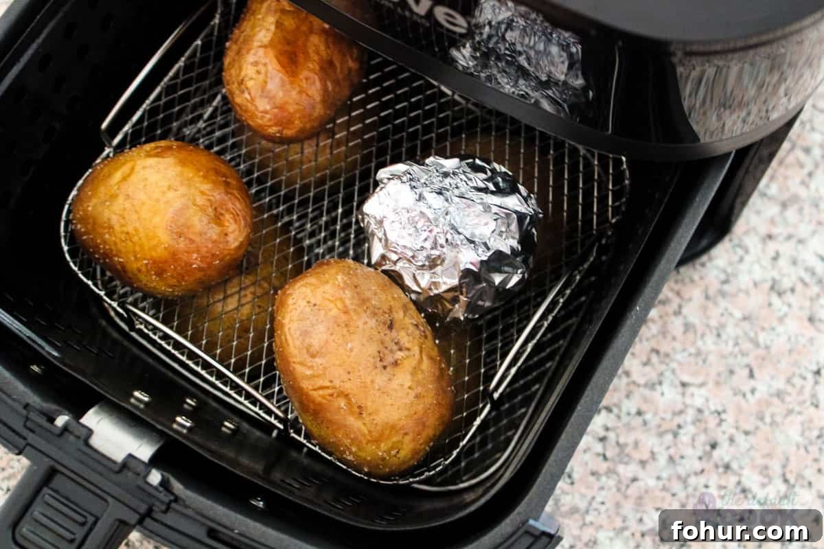 Creamy Garlic Mashed Potatoes Made in an Air Fryer 5 Cooked potatoes and head of garlic wrapped in aluminum foil in a basket style air fryer.