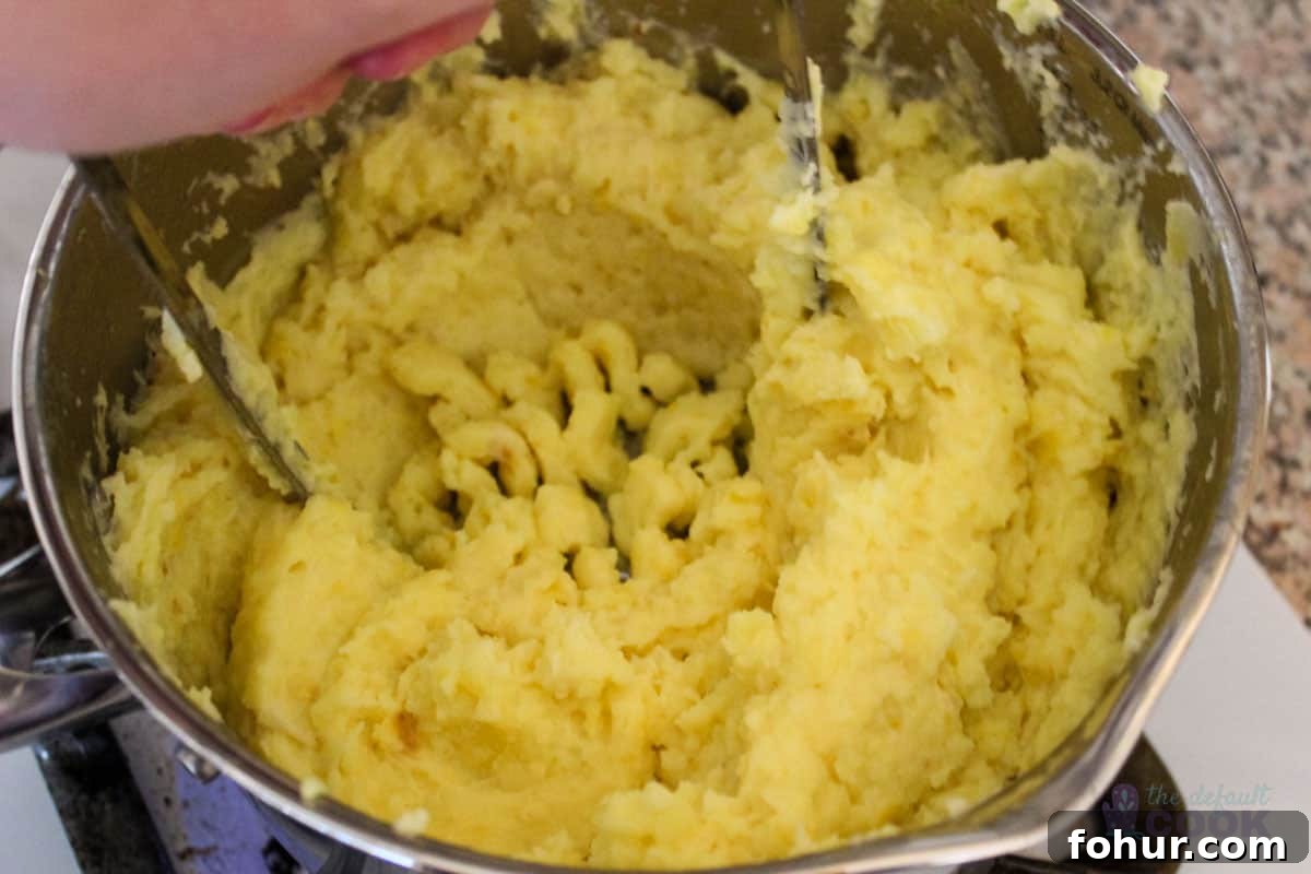 Creamy Garlic Mashed Potatoes Made in an Air Fryer 8 Hand mashing the potatoes in a pan.