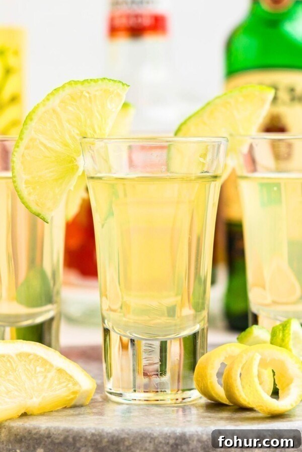 Green tea shots in small shot glasses garnished with lime wedges on a marble serving tray.