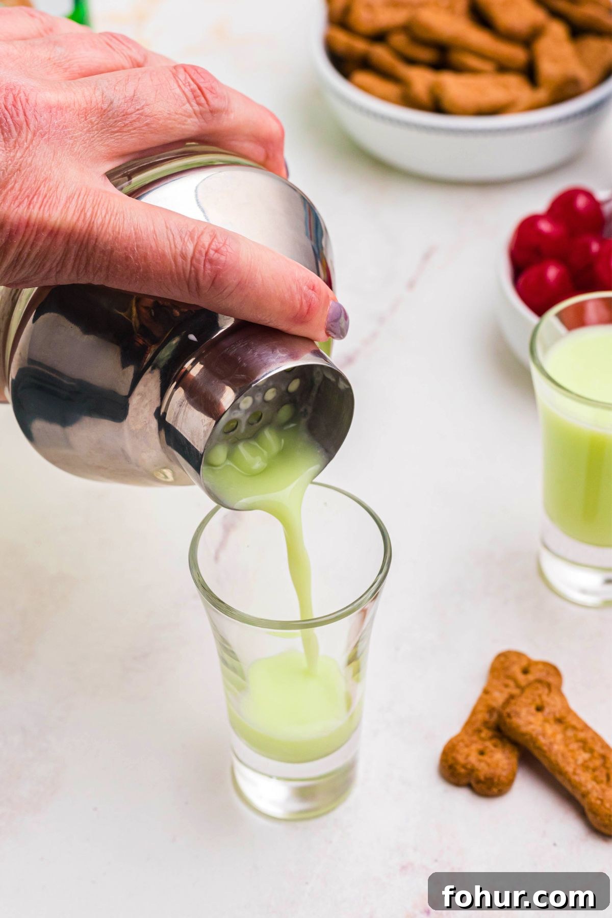 Scooby Snack Shot Cocktail Recipe 6 Green scooby shot being strained into small shot glass on a marble table.