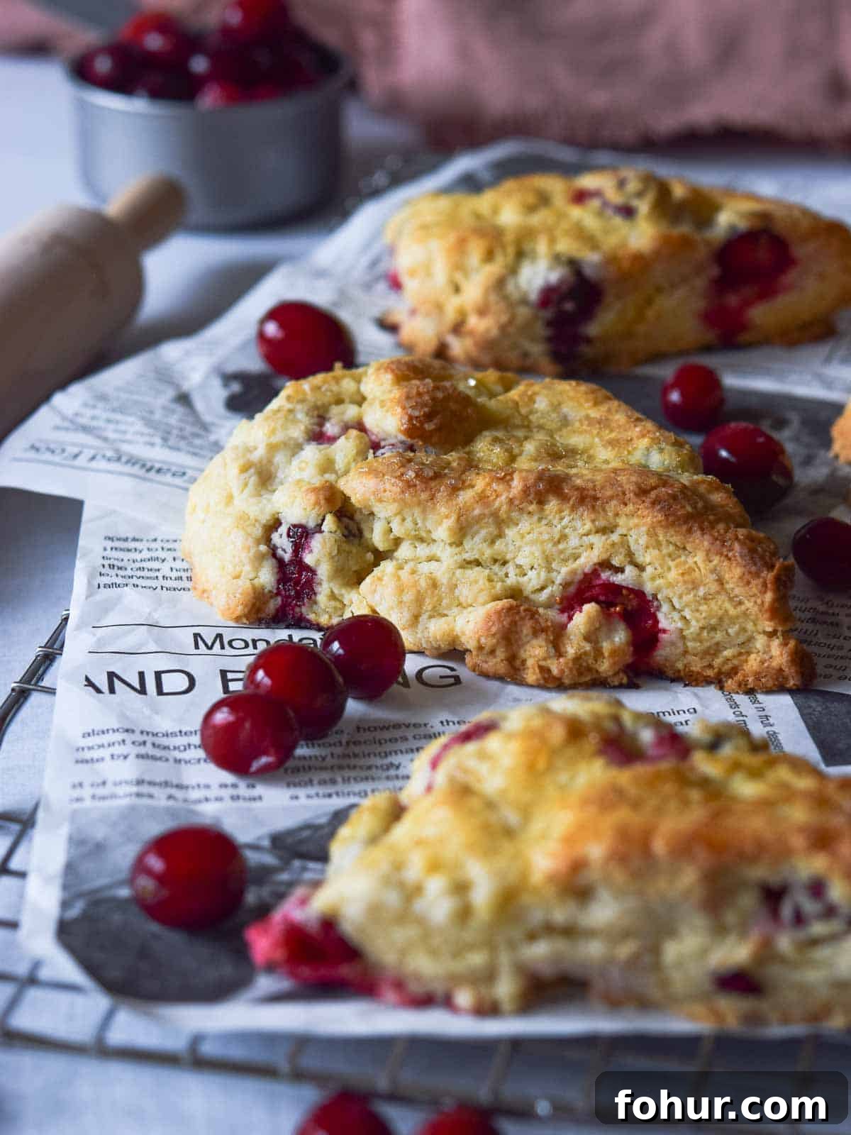 Tender Cranberry Orange Cream Scones Recipe 2 Angled view of cranberry orange scones on a cooling rack with scattered cranberries.