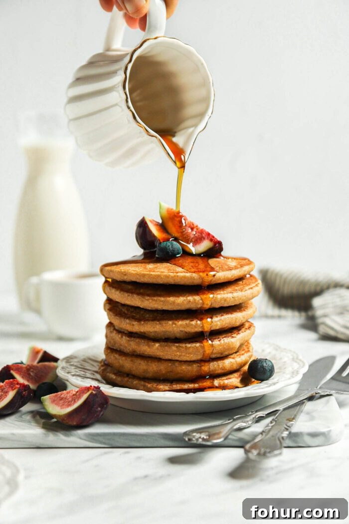 Fluffy Vegan Oat Flour Pancakes (Banana-Free) 6 Hand pouring maple syrup from a small container over a stack of healthy oatmeal pancakes.