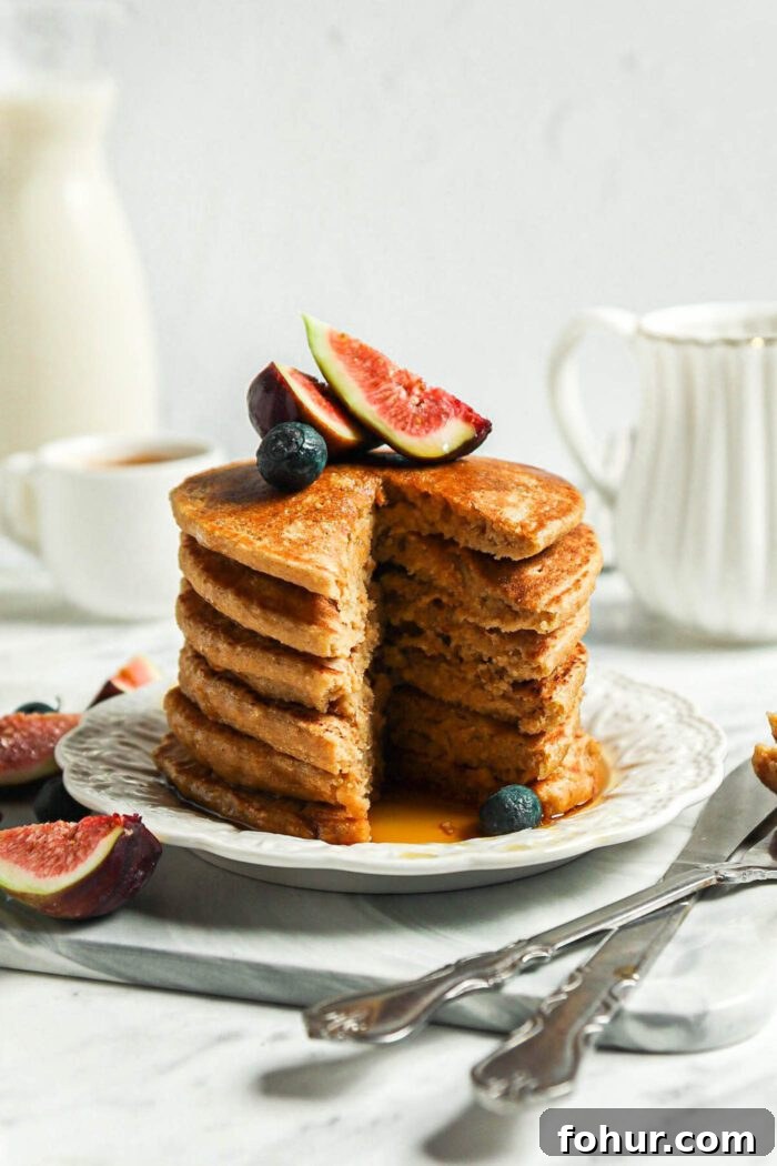 Fluffy Vegan Oat Flour Pancakes (Banana-Free) 7 Stack of thick vegan oat flour pancakes topped with blueberries and figs on a small plate.The stack has a slice taken from it so you can see the inside texture of the pancakes.